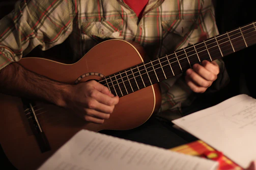 An overhead shot of hands playing an acoustic guitar with sheet music scattered nearby.
