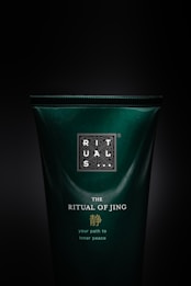 A dark green bottle of 'The Ritual of Jing' with text emphasizing its purpose of providing a path to inner peace. The branding is elegant with gold and white lettering, offering a sense of luxury and tranquility.