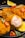 Crispy fried chicken pieces are garnished with red chili slices and rosemary sprigs on a black plate. A wedge of fresh lemon is placed alongside the chicken, adding a pop of color. The texture of the golden-brown batter is evident, with one piece showing the juicy cooked interior.