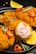 Crispy fried chicken pieces are garnished with red chili slices and rosemary sprigs on a black plate. A wedge of fresh lemon is placed alongside the chicken, adding a pop of color. The texture of the golden-brown batter is evident, with one piece showing the juicy cooked interior.