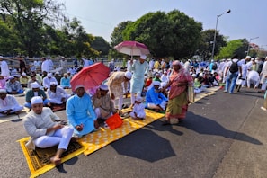 A group of people gathered for Eid prayers in an open field under a clear sky.