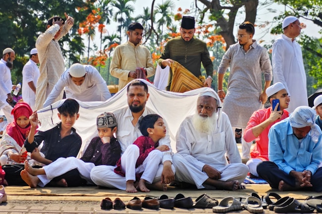A group of smiling families gathered in prayer under a sunny sky at a community picnic.