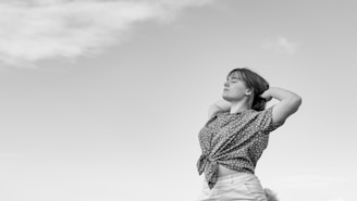 a woman standing in a field with her arms behind her head