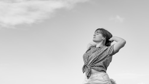 a woman standing in a field with her arms behind her head