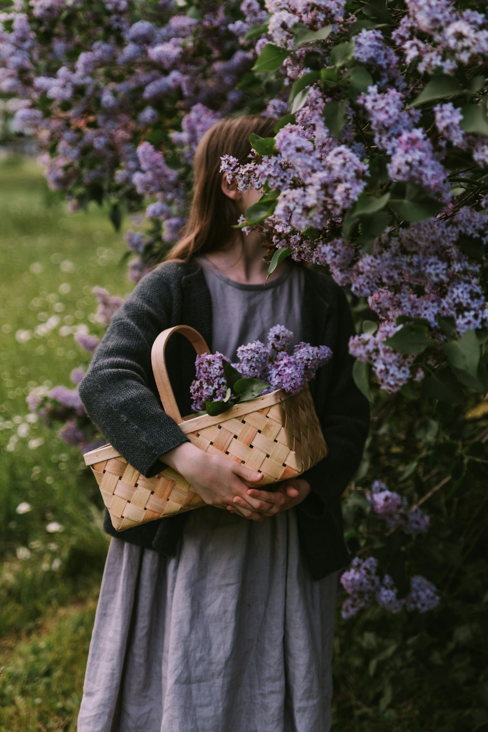 a woman standing in front of a bush with purple flowers