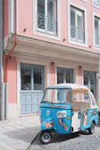 A vibrant turquoise tuk tuk parked by the sparkling Adriatic Sea under a clear blue sky.