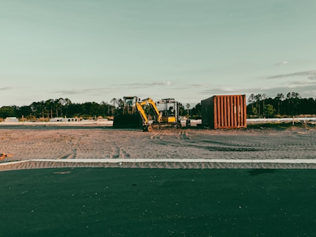 An excavator smoothing earth on a construction site surrounded by pine trees.