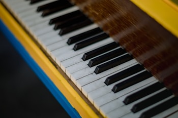 A close-up view of a piano keyboard, highlighting the black and white keys in a diagonal arrangement. The piano casing features vibrant yellow and blue colors.