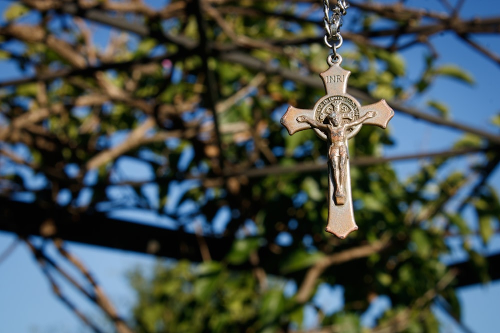 a cross hanging from a chain in front of a tree