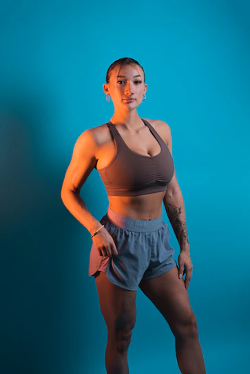 A confident woman in sleek fitness wear standing strong against a minimalist gray and pink backdrop.