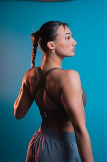 A woman with a braided hairstyle wearing athletic clothing stands against a blue background, looking to the side with a relaxed expression.