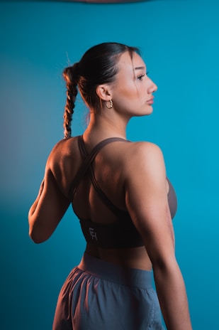 A woman with a braided hairstyle wearing athletic clothing stands against a blue background, looking to the side with a relaxed expression.