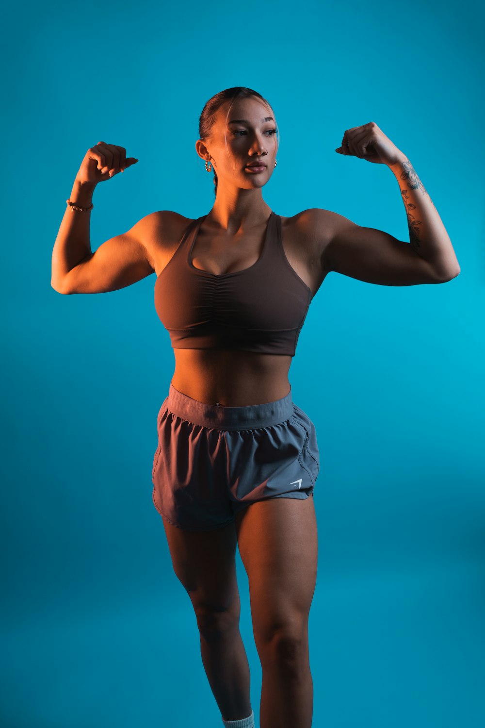 uma mulher com um top de sutiã esportivo e shorts flexionando os músculos