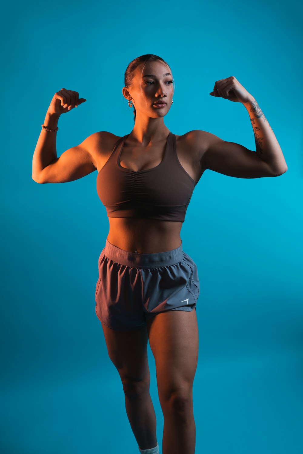 a woman in a sports bra top and shorts flexing her muscles