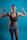 A woman with braided hair poses confidently with both arms flexed against a blue background. She is wearing a brown sports bra and gray shorts, showcasing her toned muscles. The lighting emphasizes her physique and creates a strong, empowering image.