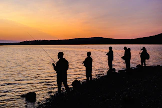 A friendly group of anglers gathered by a peaceful lake at sunset.