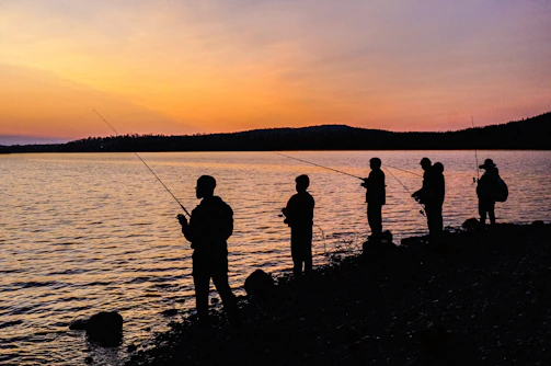 A friendly group of anglers gathered by a peaceful lake at sunset.