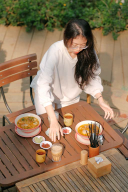 A rustic wooden table set with steaming bowls of thukpa, colorful momos, and a pot of herbal tea, sunlight filtering through leaves.