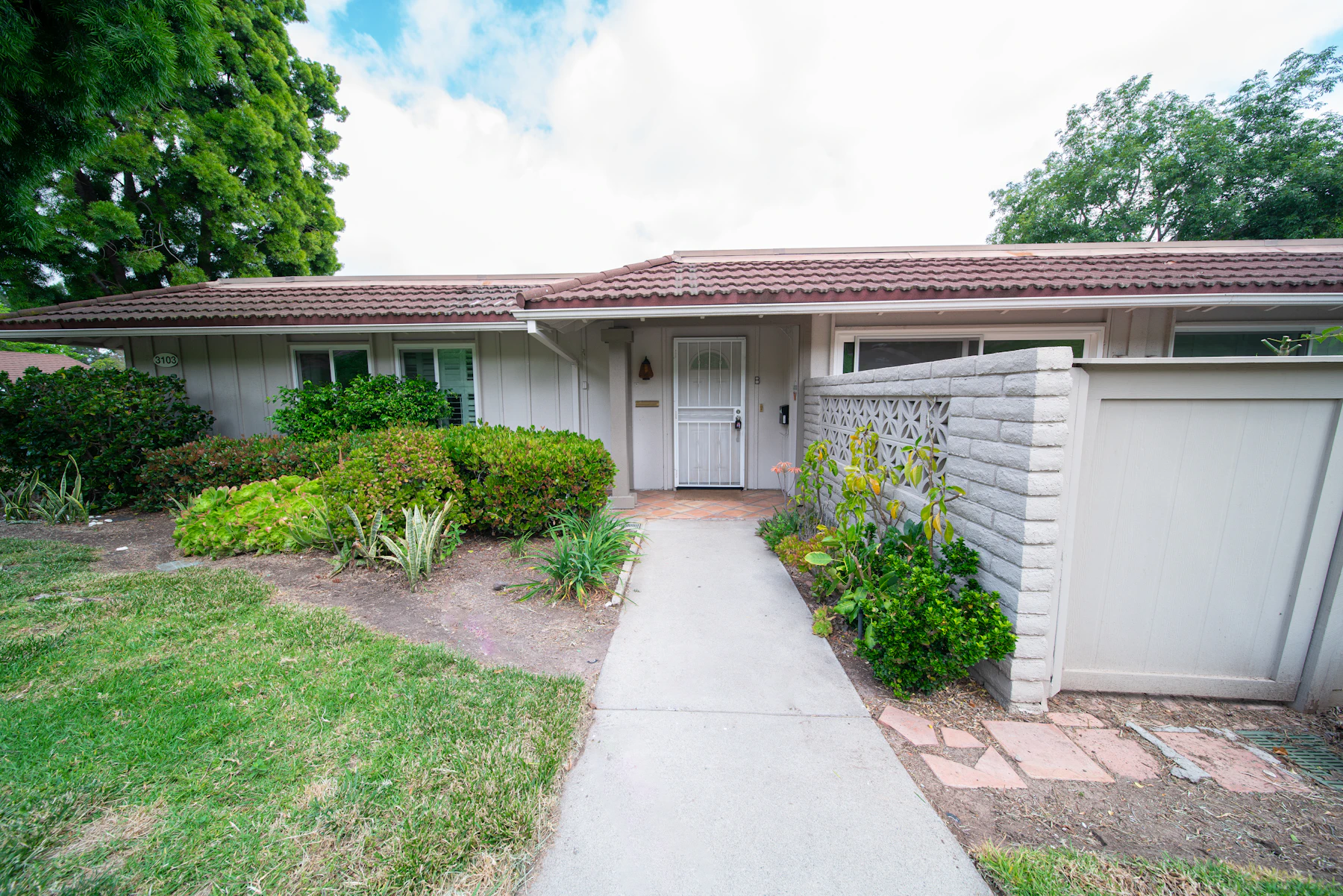 A single-story 1960s ranch home in Fair Oaks with a low tile roof, mature shade trees, and a breeze-block privacy wall in late-afternoon light
