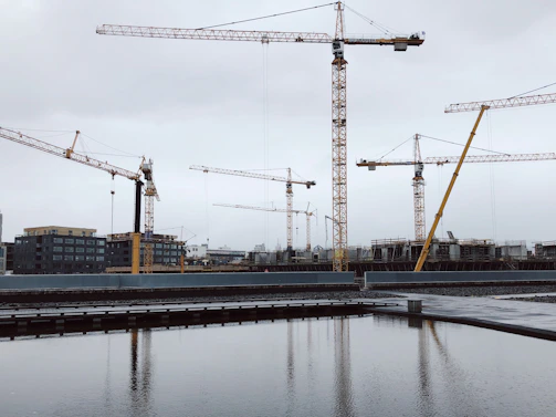 Construction team reviewing blueprints on a building site with cranes in the background.