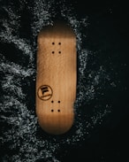 A wooden skateboard deck with screw holes is placed against a dark, textured background. The word 'FORWARD' and a logo are visible on the deck.