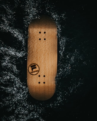 A wooden skateboard deck with screw holes is placed against a dark, textured background. The word 'FORWARD' and a logo are visible on the deck.