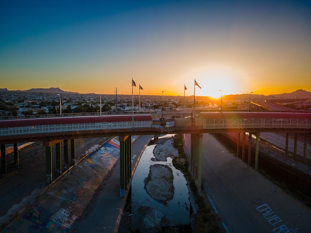 the sun is setting over a bridge over a river