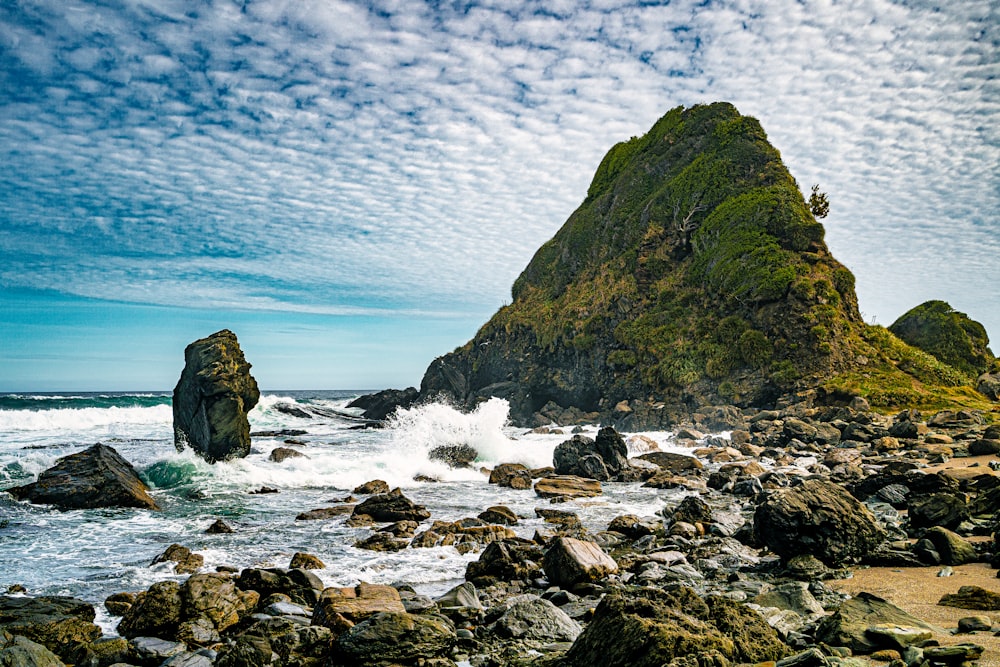 a large rock sticking out of the ocean next to a beach