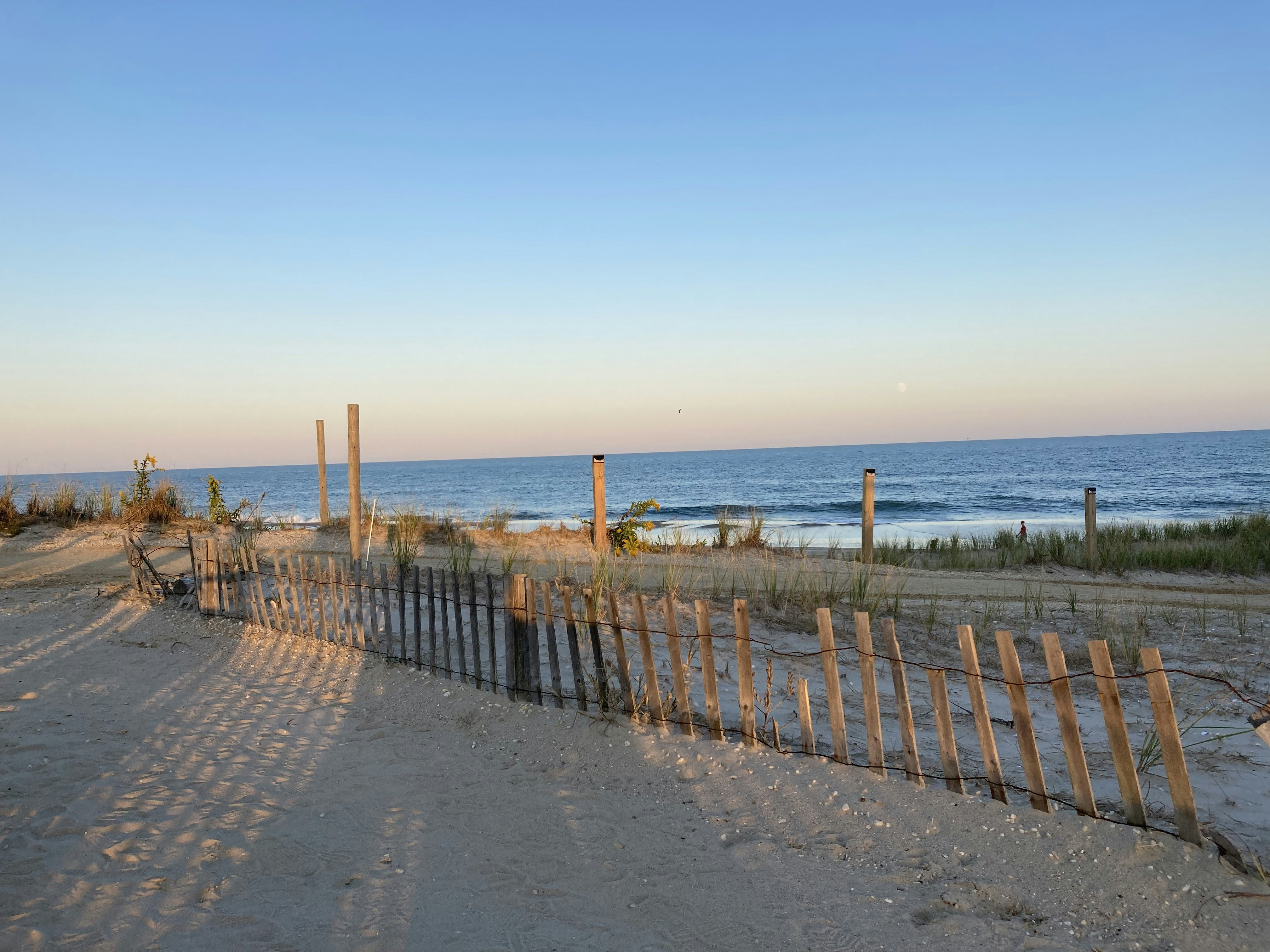 a sandy beach next to the ocean with a wooden fence