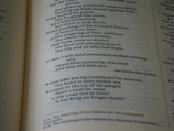 A close-up view of a page from a Bible, displaying text with a focus on specific verses. The text is in a serif font, printed in black on white paper. The page is slightly tilted, and the lighting casts subtle shadows, adding depth to the text.