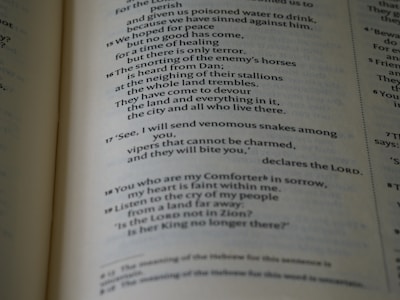 A close-up view of a page from a Bible, displaying text with a focus on specific verses. The text is in a serif font, printed in black on white paper. The page is slightly tilted, and the lighting casts subtle shadows, adding depth to the text.