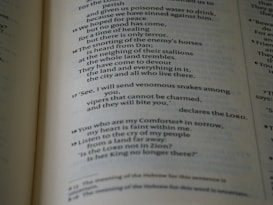 A close-up view of a page from a Bible, displaying text with a focus on specific verses. The text is in a serif font, printed in black on white paper. The page is slightly tilted, and the lighting casts subtle shadows, adding depth to the text.