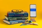 a stack of books and a cell phone on a yellow background