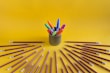 Colorful pens, markers, and art supplies neatly arranged against a bright yellow backdrop.