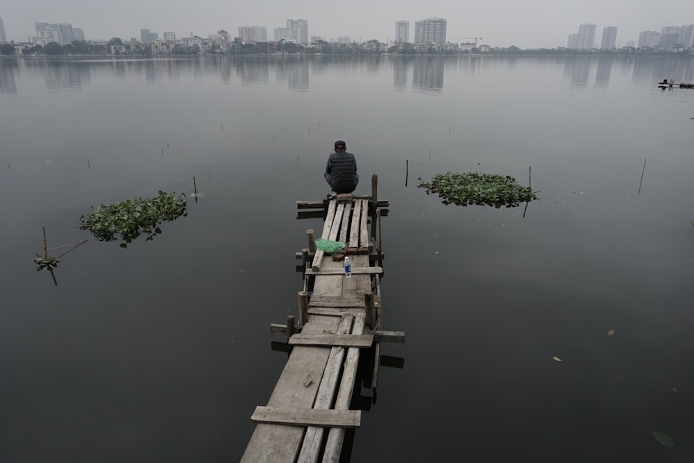 a man sitting on a wooden dock in the middle of a lake