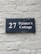 A dark blue rectangular sign with white lettering that reads '27 Painter's Cottage' is mounted on a light gray brick wall. The wall has a rough texture with visible bricks and mortar lines.