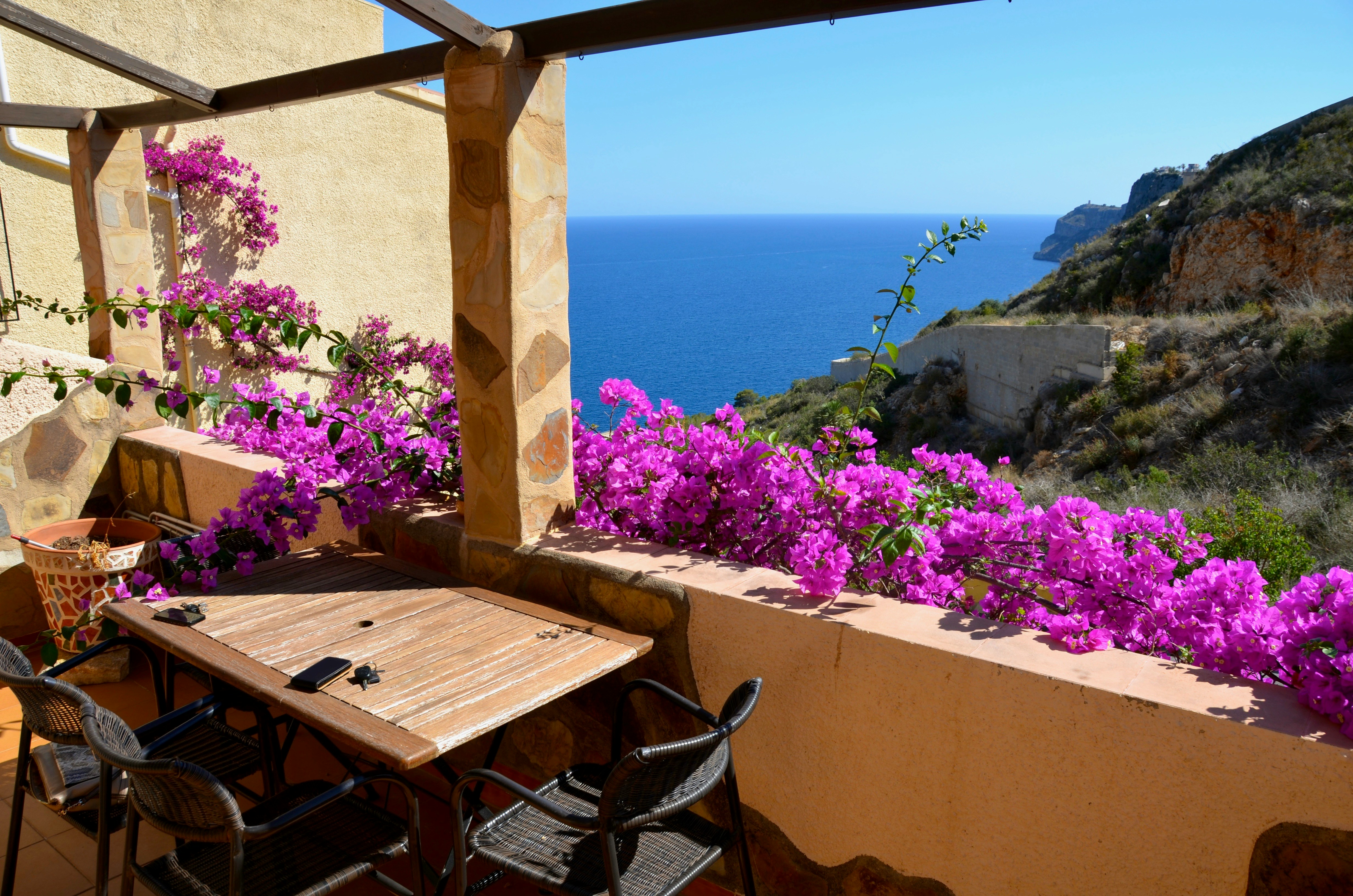 a table and chairs on a balcony with purple flowers