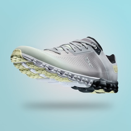 A single sports shoe is prominently displayed against a seamless, light turquoise background. The shoe features a sleek design with a gradient of light gray to dark gray tones, and is equipped with a distinctive CloudTec sole for cushioning. The branding logo is subtly visible on the side.