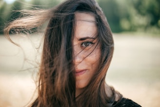 A raw portrait of a woman standing outdoors with soft natural light and a cluttered background.