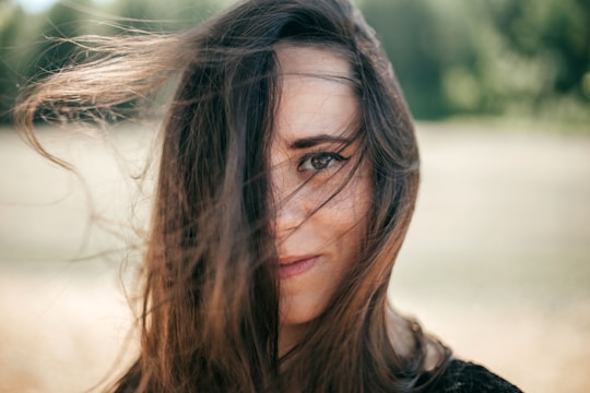 A raw portrait of a woman standing outdoors with soft natural light and a cluttered background.