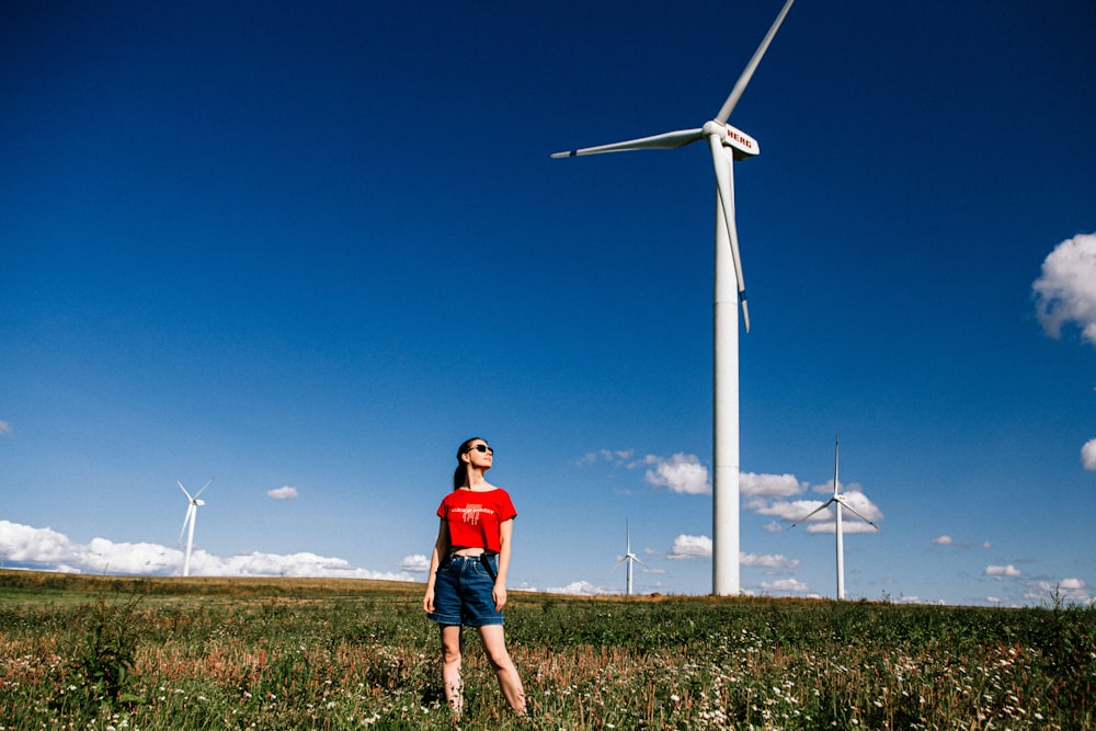 a woman standing in a field next to a wind turbine