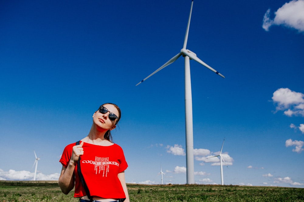 a woman in a red shirt standing in front of a wind turbine