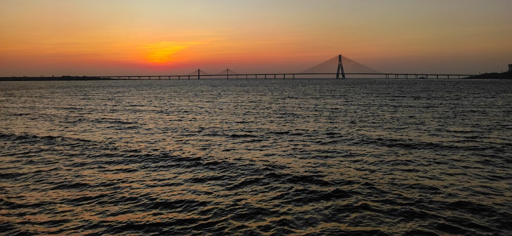 the sun is setting over the water with a bridge in the background