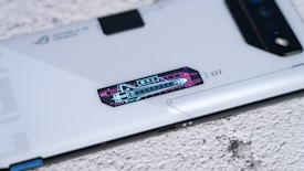 A sleek, modern smartphone with futuristic design elements and a digital display panel showing graphics and numbers, placed on a textured surface.