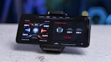 A smartphone mounted on a stand displays a screen showing performance metrics including CPU temperature, GPU temperature, memory usage, and cooler information. The interface design uses a futuristic style with red and blue accents.