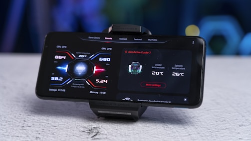 A smartphone mounted on a stand displays a screen showing performance metrics including CPU temperature, GPU temperature, memory usage, and cooler information. The interface design uses a futuristic style with red and blue accents.