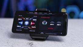 A smartphone mounted on a stand displays a screen showing performance metrics including CPU temperature, GPU temperature, memory usage, and cooler information. The interface design uses a futuristic style with red and blue accents.