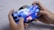 A person is holding a smartphone horizontally, playing a racing video game. The screen shows a high-speed race scene with a car emitting sparks. The hands are gripping the device tightly, indicating focus and engagement in the game.