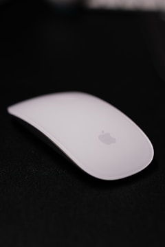 A sleek white computer mouse with a minimalist design placed against a dark background, featuring a subtle logo in the center.