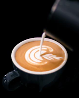 Close-up of artisan barista pouring latte art in a sleek black and gold coffee cup.